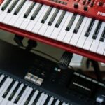 Vertical shot of red and black electronic keyboards in a home studio setting.