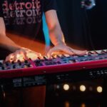 Close-up of a musician playing a keyboard on stage with vibrant light effects creating a dynamic atmosphere.